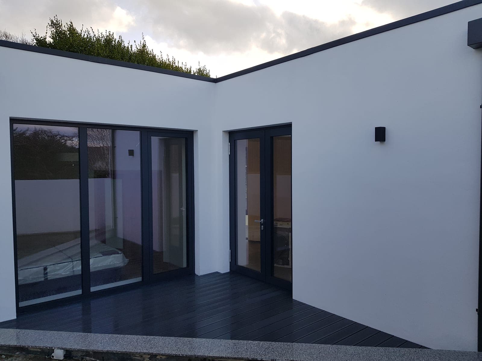 White rendered walls with black-framed glazed doors onto dark decking