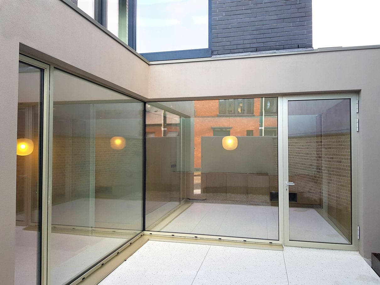 Frameless glazed corner opening onto a paved courtyard