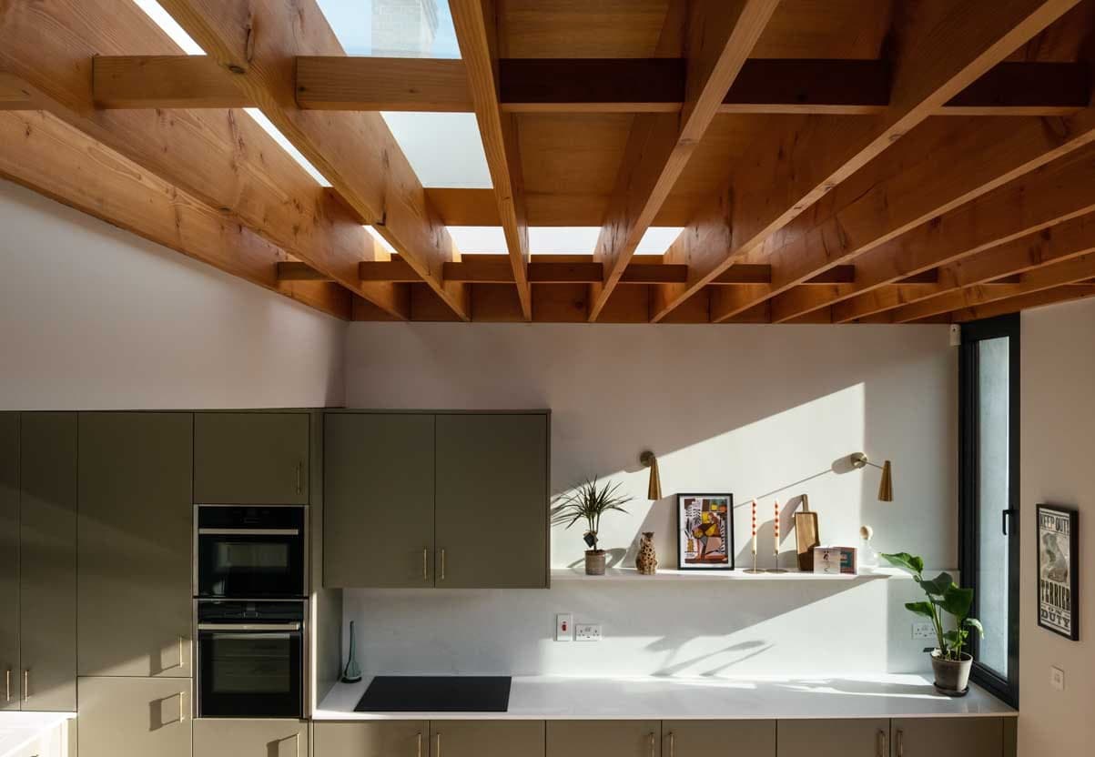 Sage green kitchen under exposed timber joists and rooflights